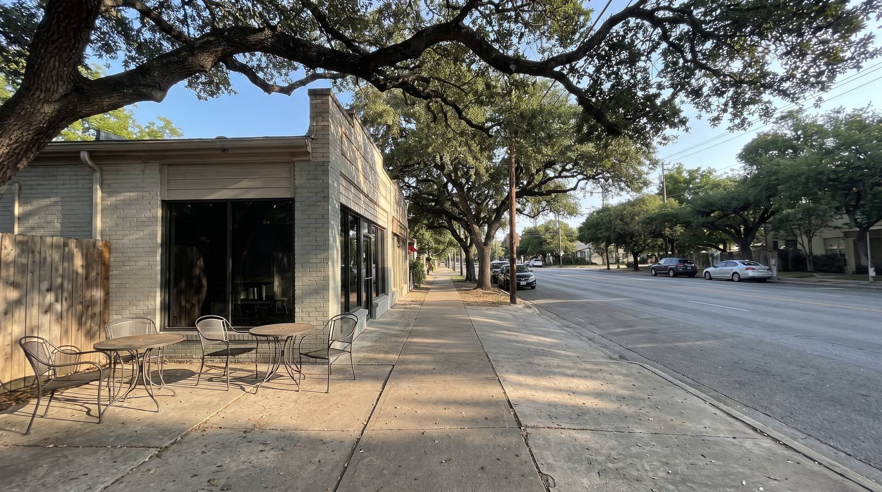 Sunny South Congress street with live oak shade and a small storefront patio in the morning